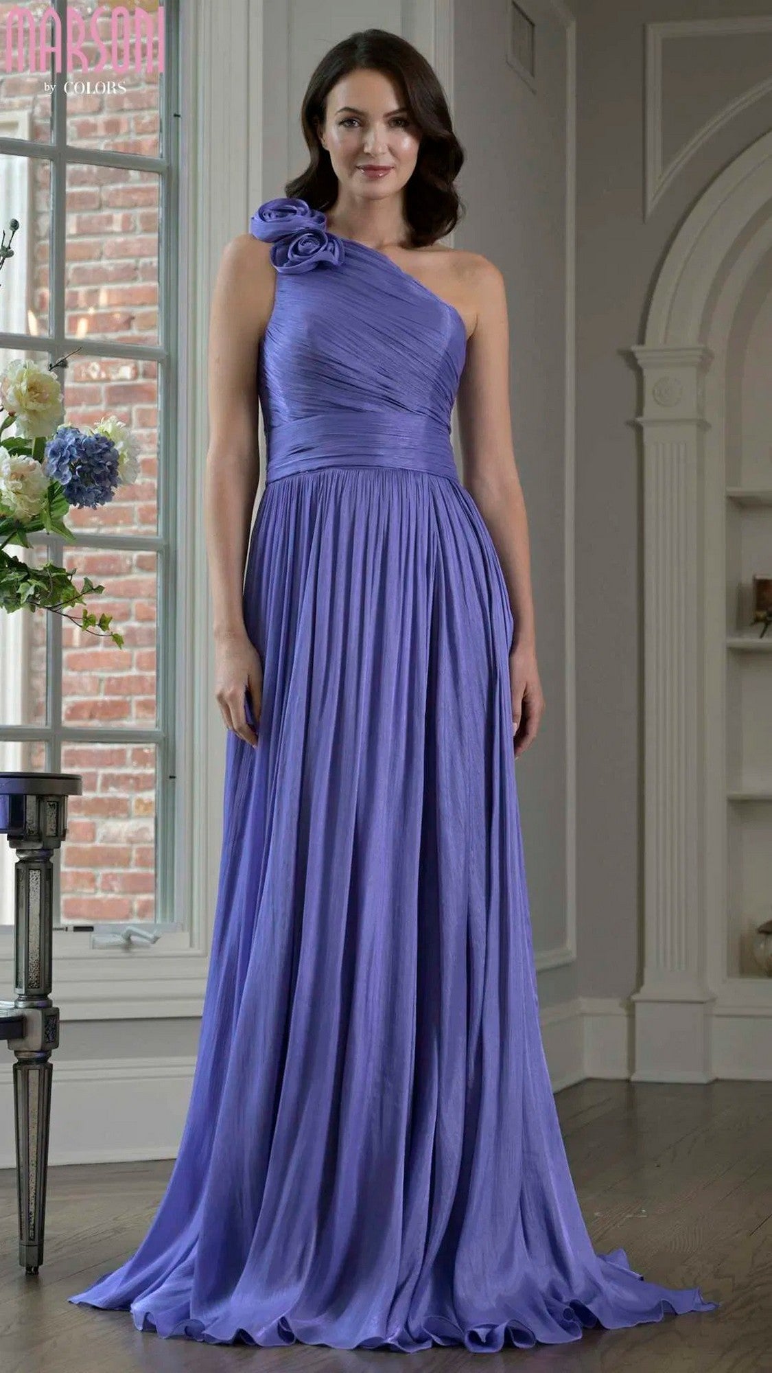 A woman stands indoors wearing the Marsoni M332 long formal dress in violet, a floor-length, one-shoulder gown adorned with elegant 3D floral embellishments on the strap.
